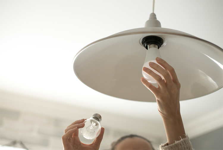 A woman replacing an incandescent bulb with an efficient LED lightbulb