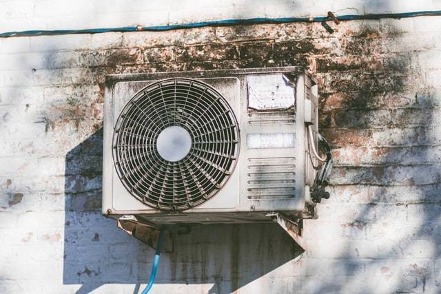 An aging air conditioning unit mounted to a wall provides the building with cooling in warm summer months